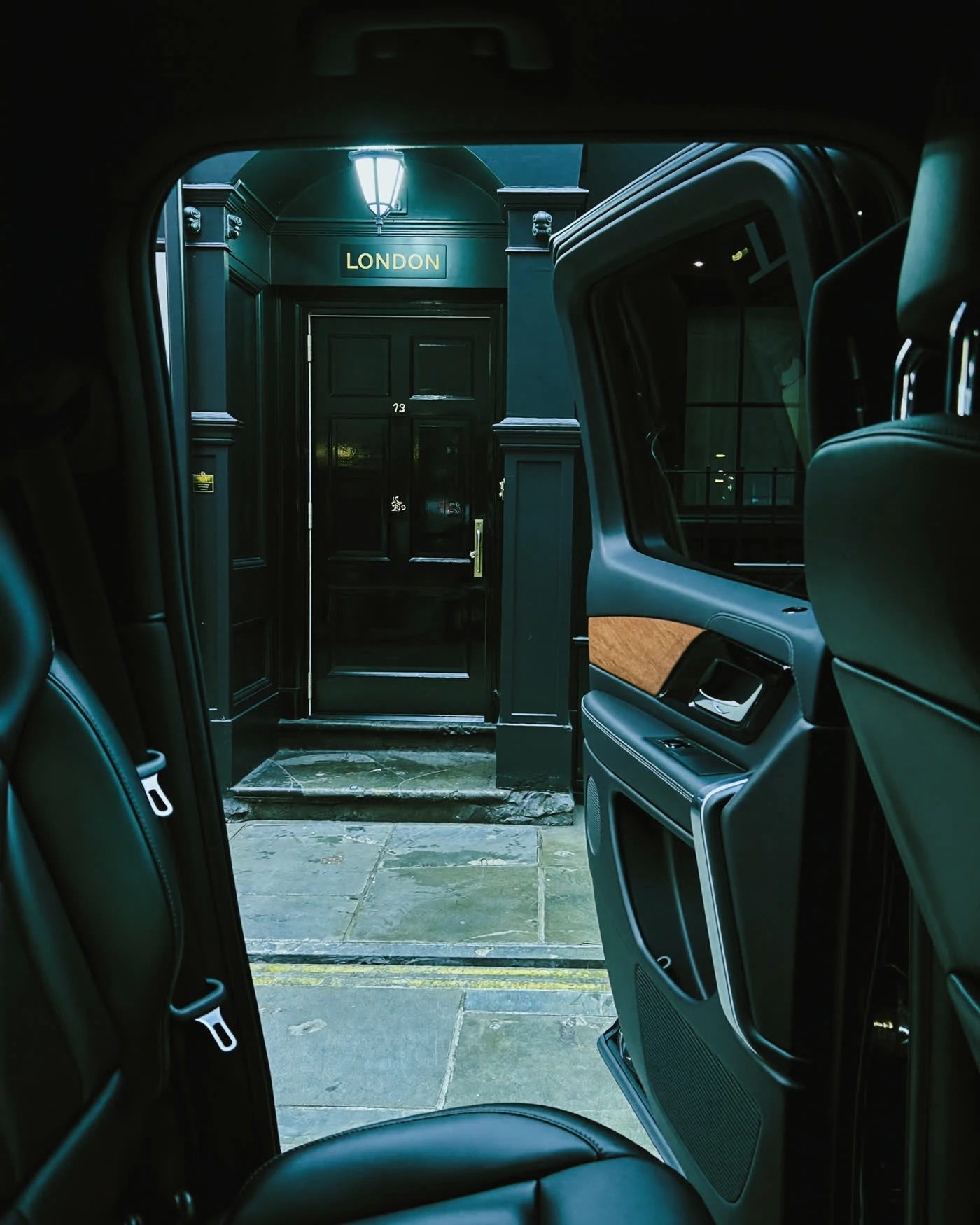 Chauffeur handling luggage door to door outside a London entrance at night