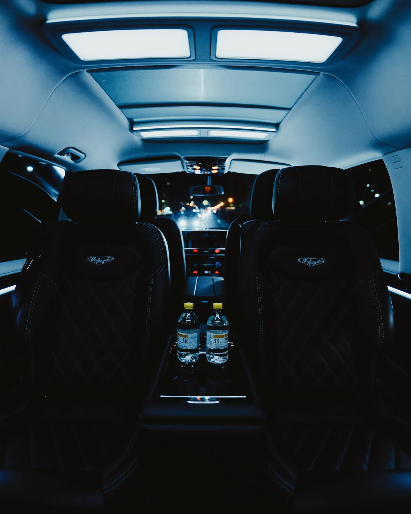 Interior of a quiet Mercedes V-Class cabin at night, privacy glass and bottled water resting on the armrest