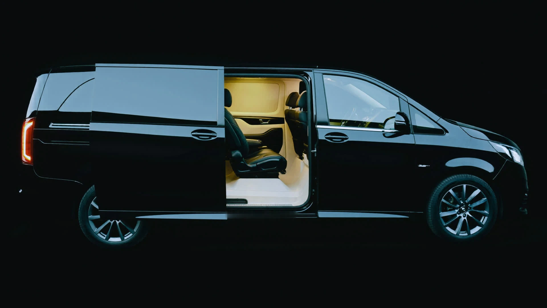 Rear door of a black Mercedes V-Class open at night, cabin ambient light glowing cool steel-blue within